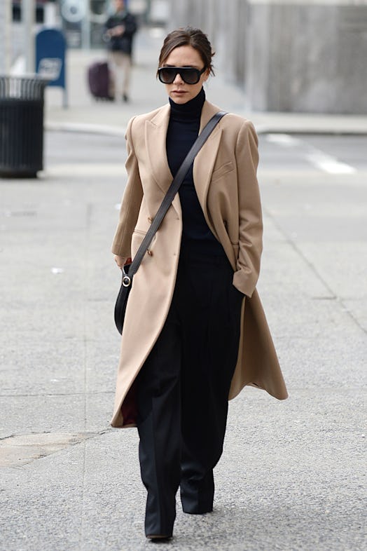 Victoria Beckham wearing a camel coat, black sunglasses, a turtleneck, and trousers.