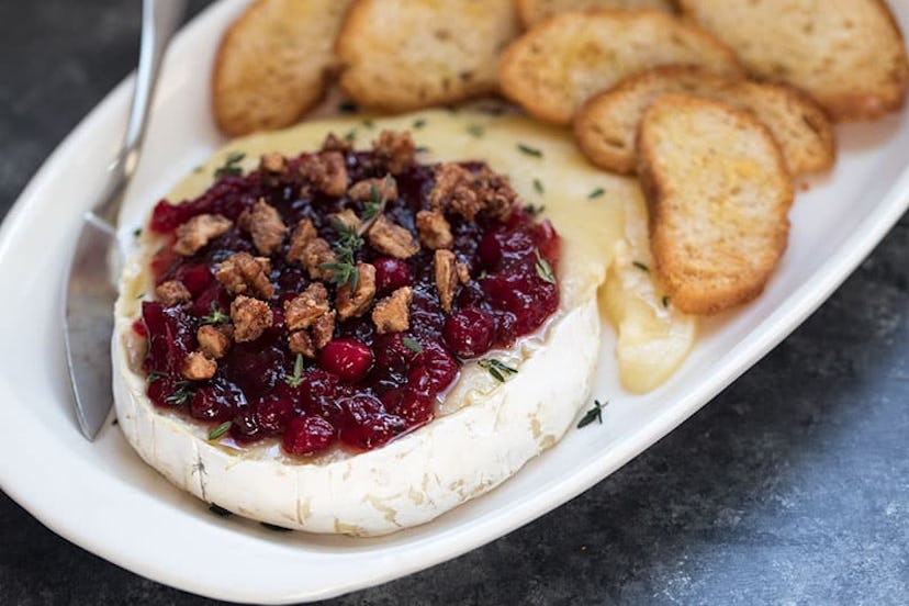 white oval plate with brie topped with cranberries and walnuts next to a bunch of slice crostinis