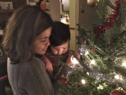 A mother holding her kid while standing next to a Christmas tree