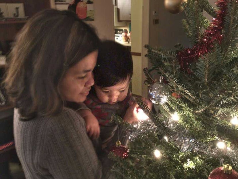 A mother holding her kid while standing next to a Christmas tree