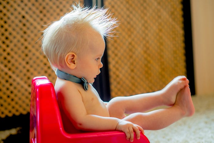 A baby wearing only a bow tie sitting on the potty 