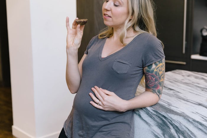 A pregnant woman eating a cookie. 