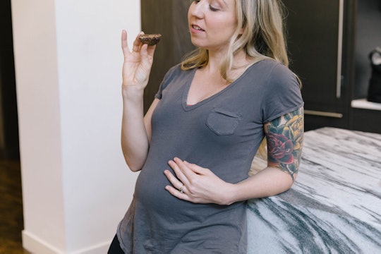 A pregnant woman eating a cookie. 