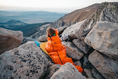 A woman in an orange Patagonia sleeping bag lying between the rocks