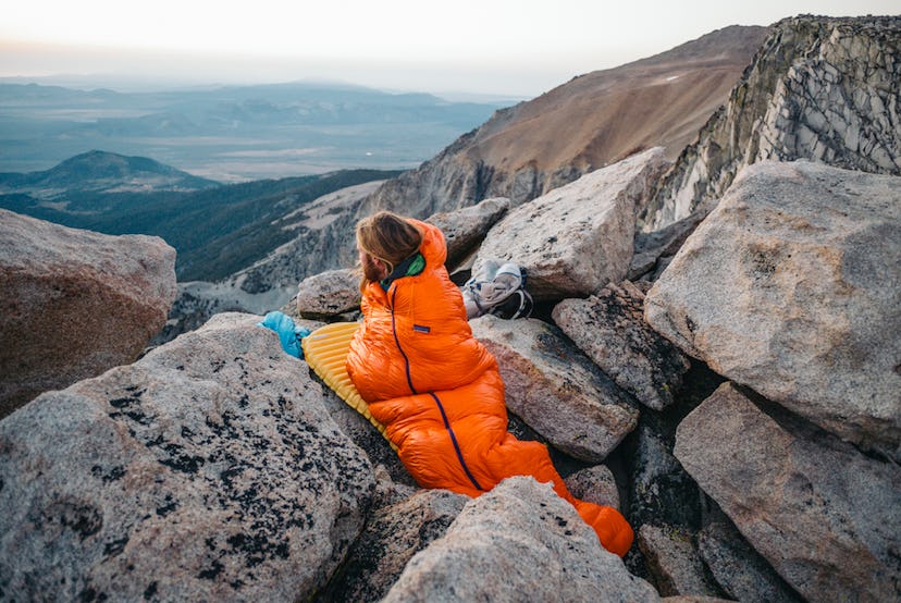 A woman in an orange Patagonia sleeping bag lying between the rocks