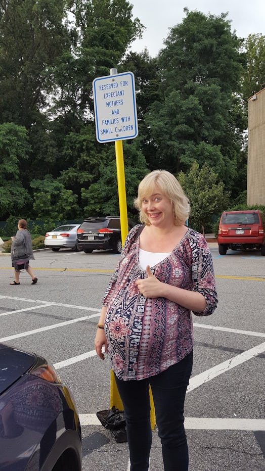 Pregnant woman standing on the parking lot and smiling while showing thumbs up