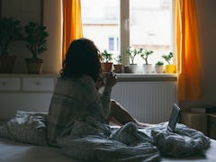 A curly-haired girl sitting on a bed looking through window.