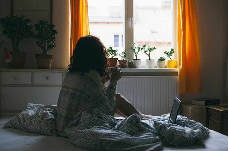 A curly-haired girl sitting on a bed looking through window.