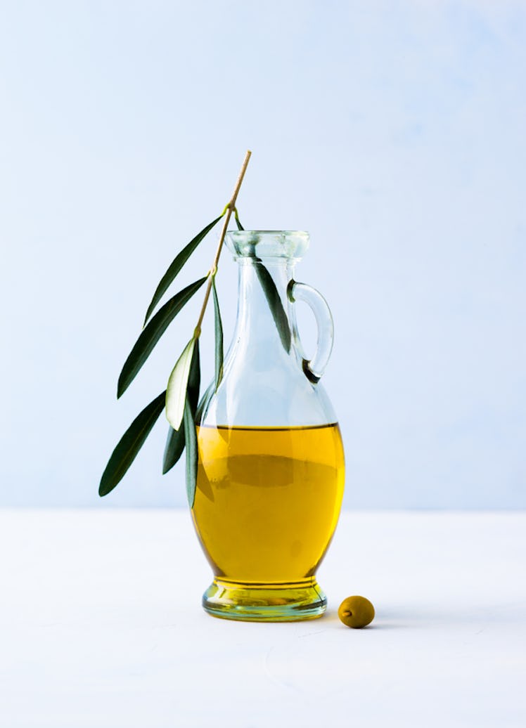 A clear glass bottle filled with Olive oil with Olive tree branch in it.