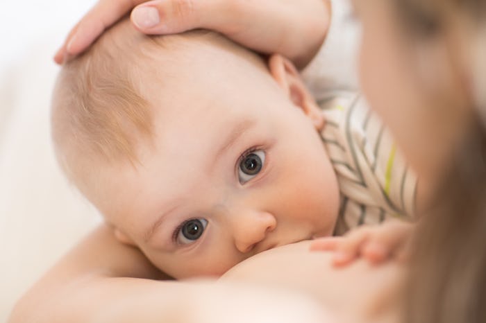 A mother breastfeeding her brown-eyed baby in a white-grey striped shirt