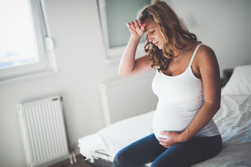 Pregnant woman sitting on edge of bed, not feeling well