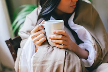 a woman wrapped up in a blanket while holding a cup of golden turmeric milk 