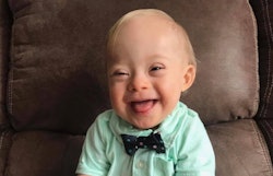 A smiling baby with down syndrome who won Gerber baby of the year in a mint shirt