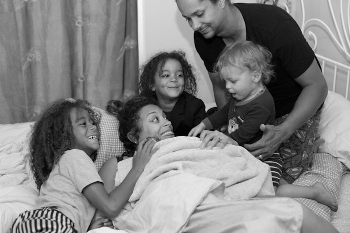 Mother, father, and three kids playing in a bed together
