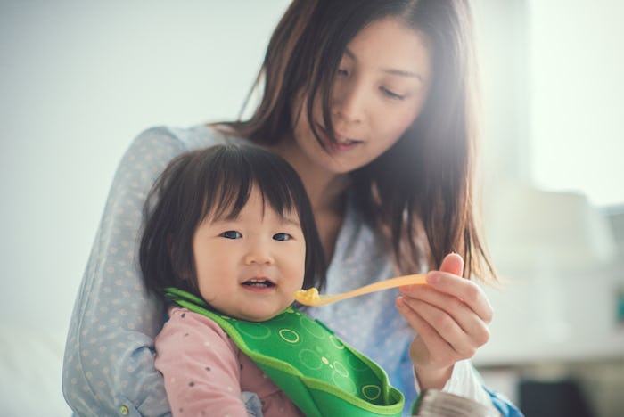 A mom holding her toddler in her lap feeding her food that she's not allergic to