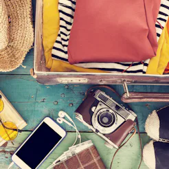 A variety of objects that are ready to be packed for a vacation next to an already full suitcase