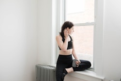 A woman in athleisure looks out the window of her studio apartment. Experts share tips for anxiety o...
