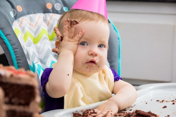 Baby in her chair eating cake with her hands and putting it all over her head