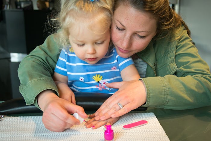 A mother holding daughter in her lap while polishing her nails.