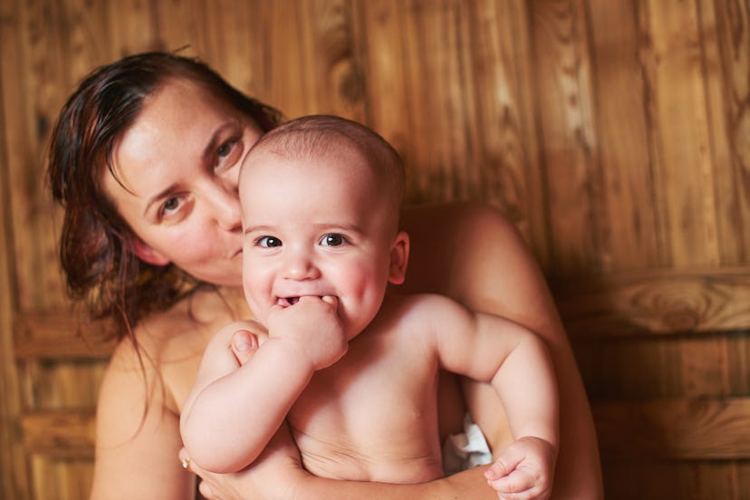 A woman in the sauna holds her baby in her arms while the baby smiles