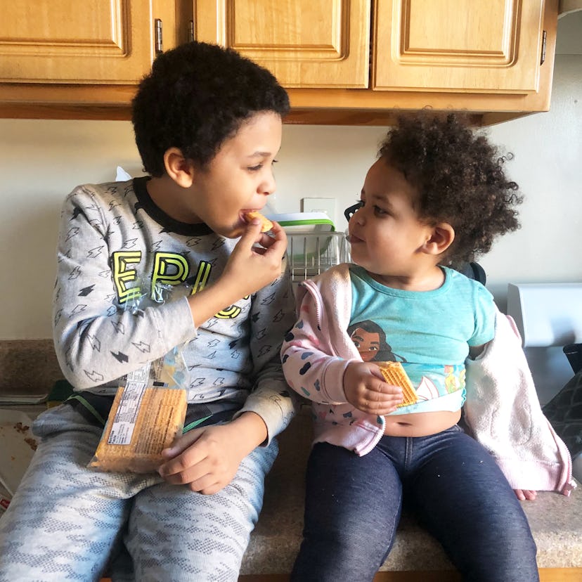 A toddler and an older kid eating biscuits while sitting on the kitchen counter