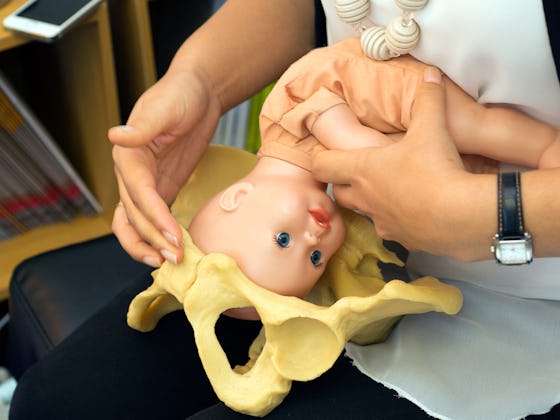 A Med Student using a doll of a baby and a model pelvis to show what giving birth is like
