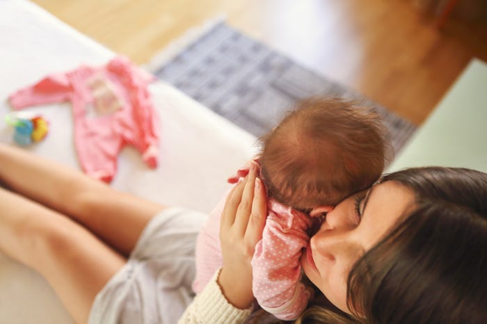 A mother sitting on a couch, holding her baby up to her face and snuggling with it