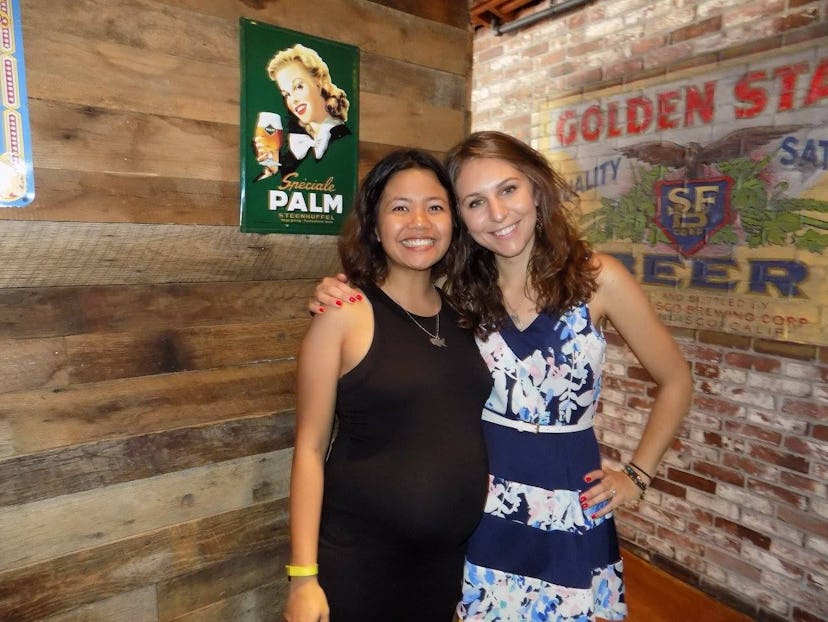 Two women are standing in a bar, dressed fancy, smiling, and hugging each other.