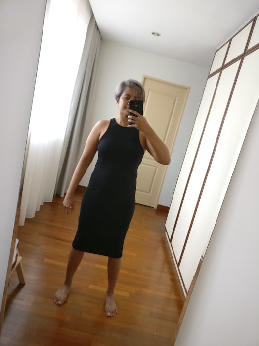 A woman taking a selfie in front of the mirror wearing a black midi dress.