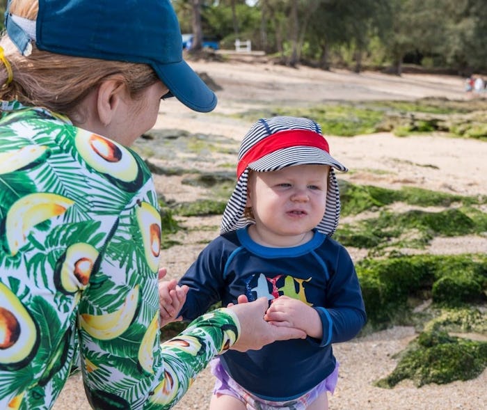 A mother holding hands of her toddler wearing a sun protective hat.