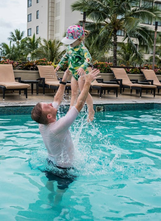 A father playing with his daughter by throwing her in the air in a pool