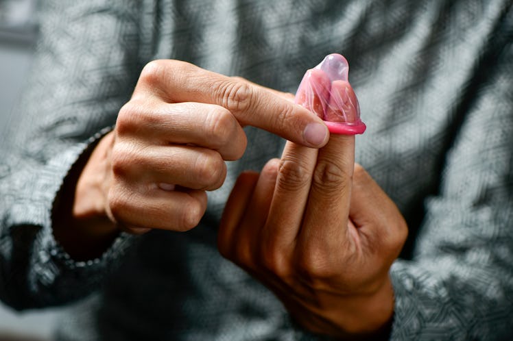 A man in a grey shirt putting a pink condom on his two fingers