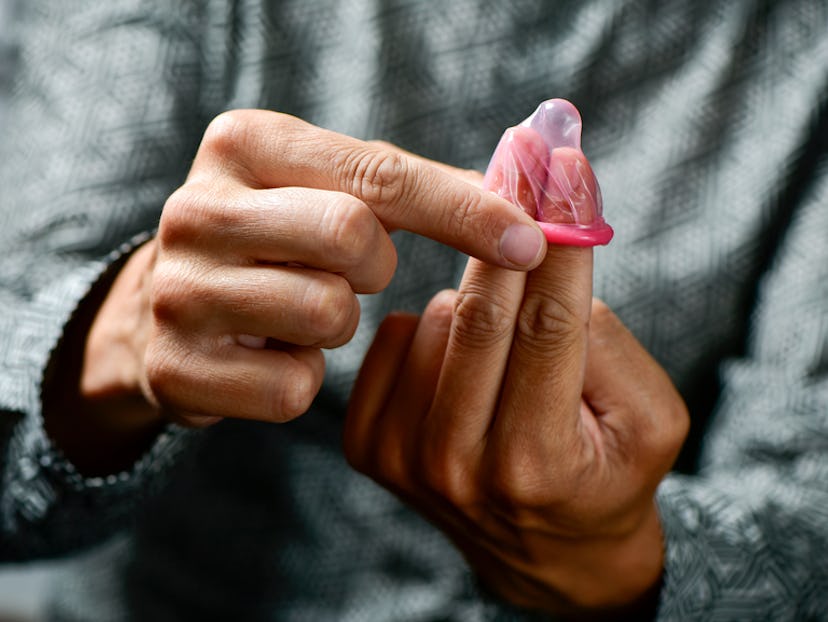 A man in a grey shirt putting a pink condom on his two fingers