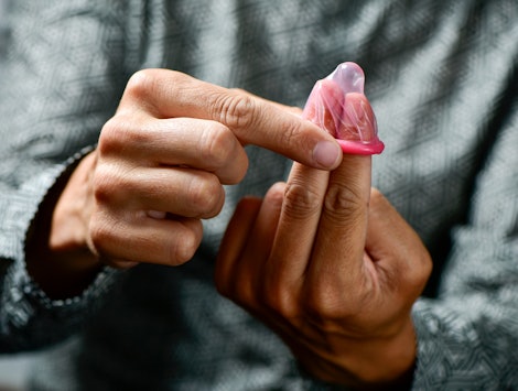 A man in a grey shirt putting a pink condom on his two fingers