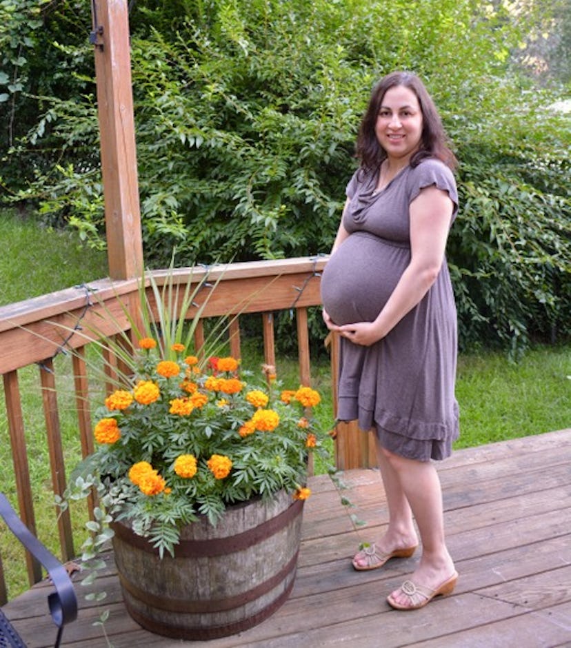 A pregnant woman posing for a picture in her gray dress next to the yellow flowers