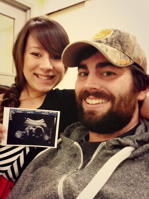 A picture of the author, smiling, with her partner as she holds up an ultrasound picture. 