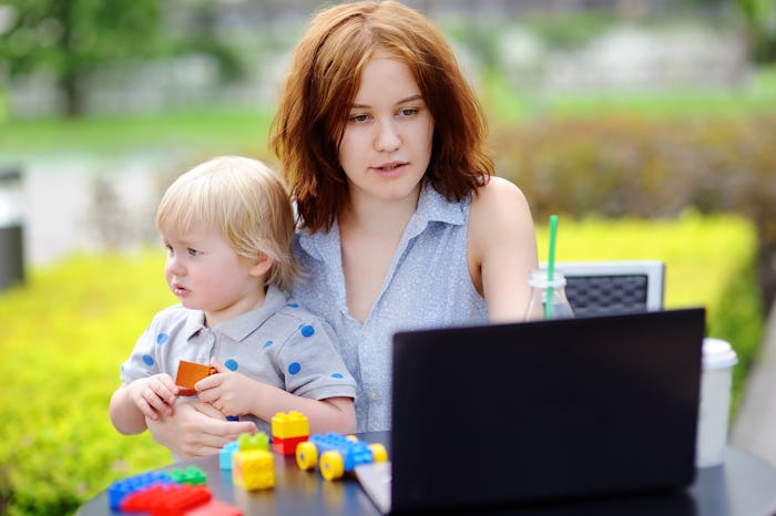 A mother looking at her laptop while holding a toddler in her lap