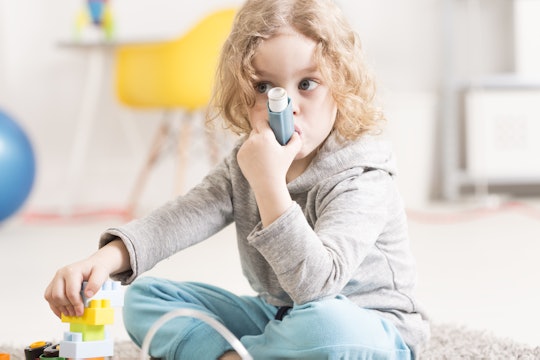 A little kid sitting on the floor of the playroom using an asthma inhaler
