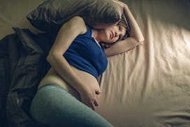 A woman struggling with pregnancy insomnia covering her head with a pillow while lying in a bed