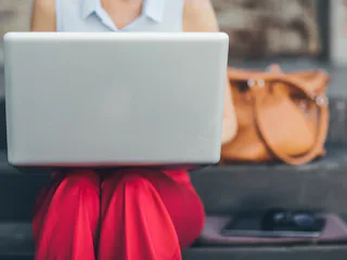 A young woman sitting on the stairs and holding her laptop in her lap.