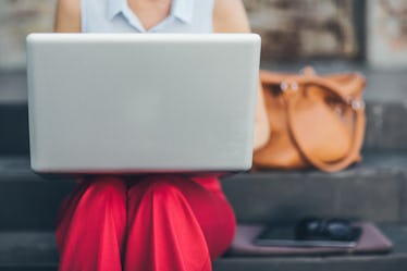 A young woman sitting on the stairs and holding her laptop in her lap.