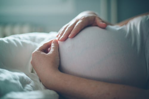 A pregnant woman holding her belly while lying in a bed