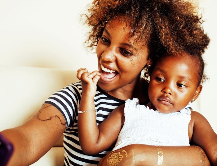 A curly-haired millennial mom taking a selfie with her child in her arms