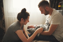 A mother kneeling in front of a dad who is holding their newborn baby in his lap