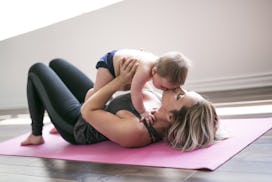 A mom lying on a yoga mat holding her newborn above her and kissing its forehead