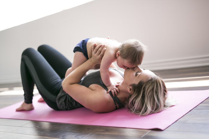 A mom lying on a yoga mat holding her newborn above her and kissing its forehead