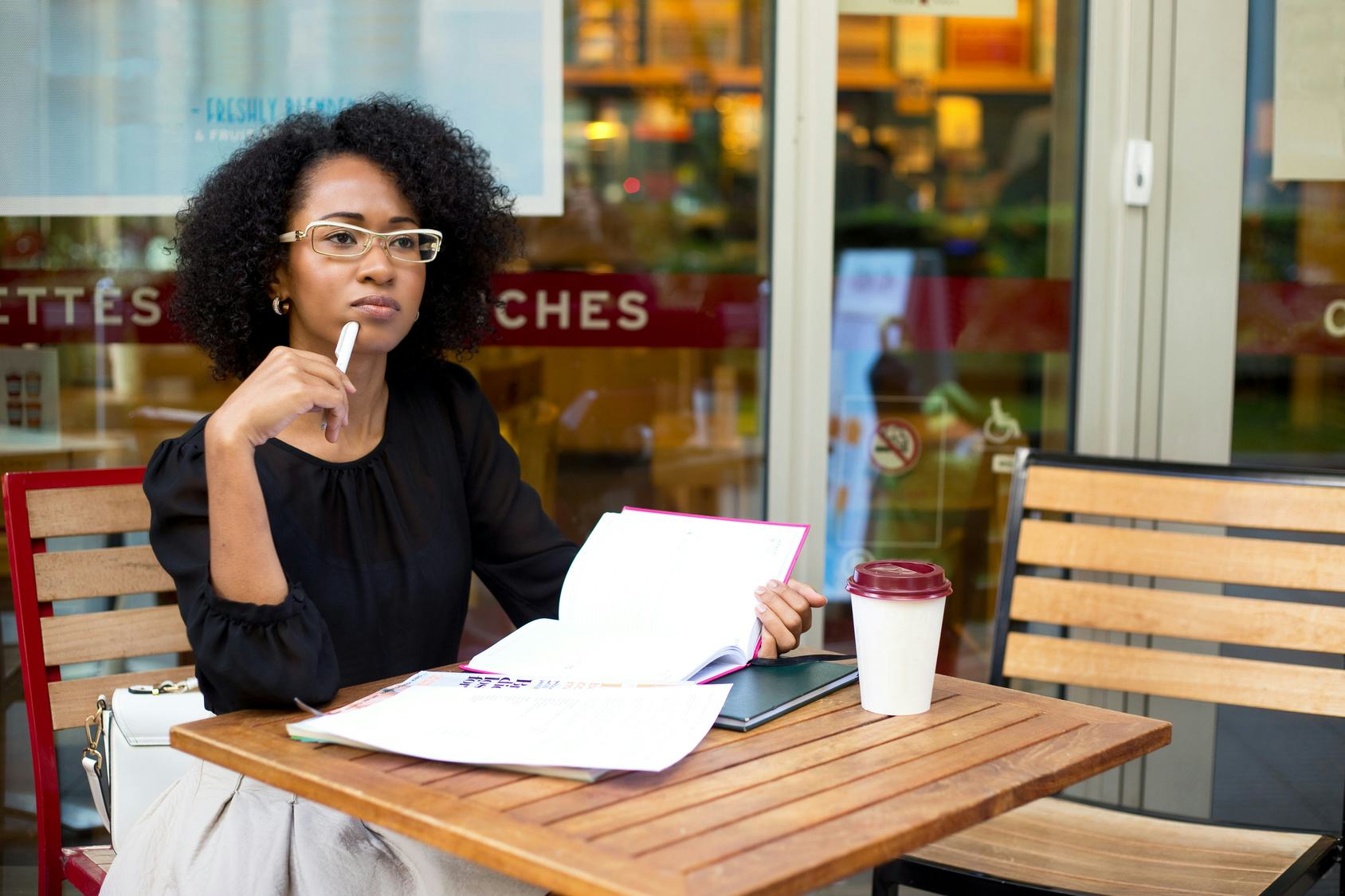 A woman sitting in a coffee shop looking straight as she feels a physical sign of ovulation