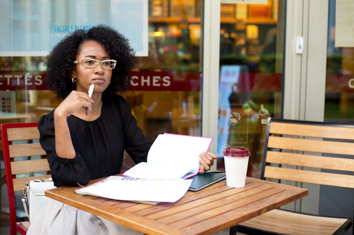 A woman sitting in a coffee shop looking straight as she feels a physical sign of ovulation