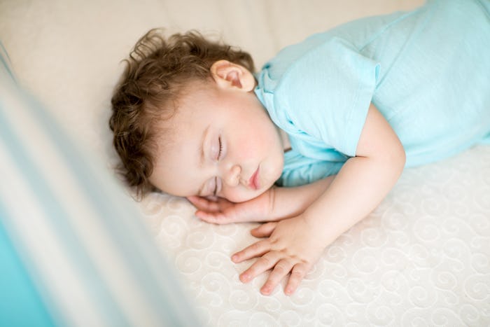 Curly-haired baby boy in a blue romper sleeping on a bed at the Day Care.