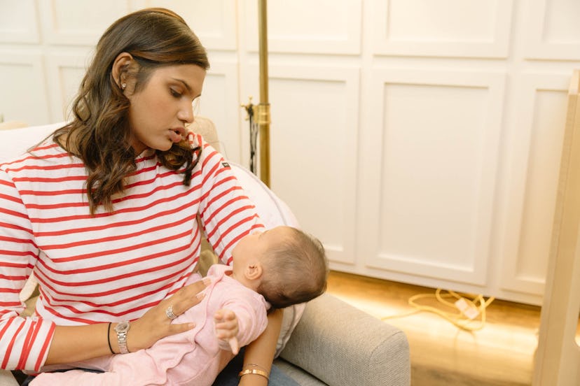 A mother in a striped red and white shirt holding her newborn baby while sitting in a chair